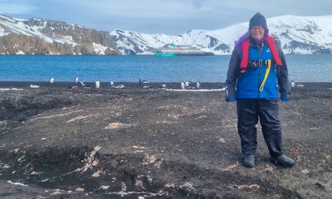 Helen from Swoop stands on a black-sand beach in Antarctica