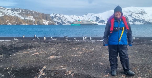 Helen from Swoop stands on a black-sand beach in Antarctica
