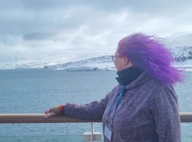 Purple-haired Helen from Swoop stands on deck and looks out across Deception Island in Antarctica