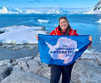 Kate from Swoop celebrates making it to her seventh continent by holding up the Antarctic flag