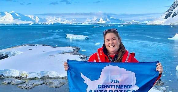 Kate from Swoop celebrates making it to her seventh continent by holding up the Antarctic flag