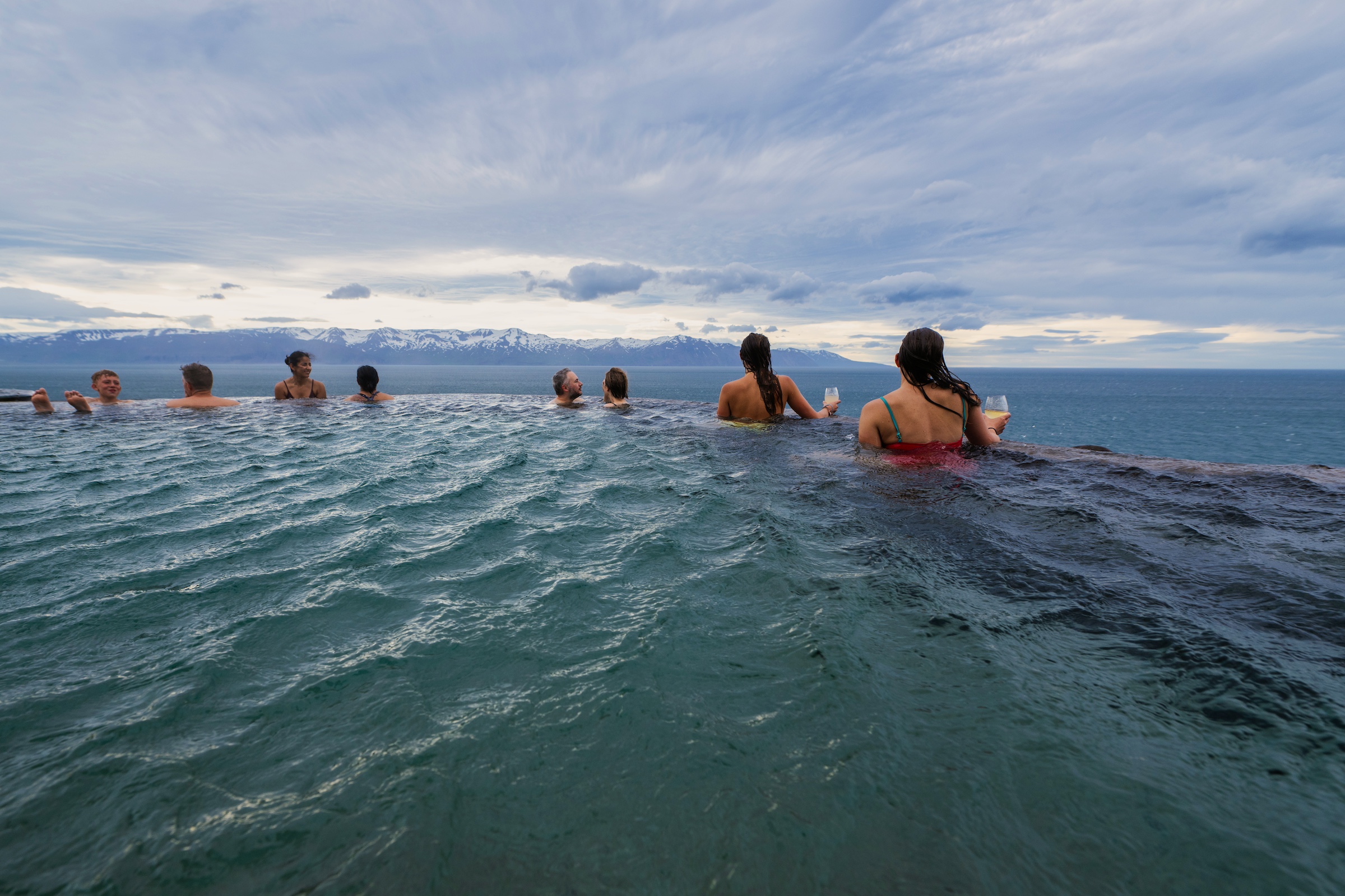 Guests relax and rejuvenate at the Húsavík GeoSea Baths in Iceland, where geothermal seawater meets stunning coastal views of Skjalfandi Bay beneath the cliffs and the Arctic Circle itself on the horizon in Húsavík, Iceland.