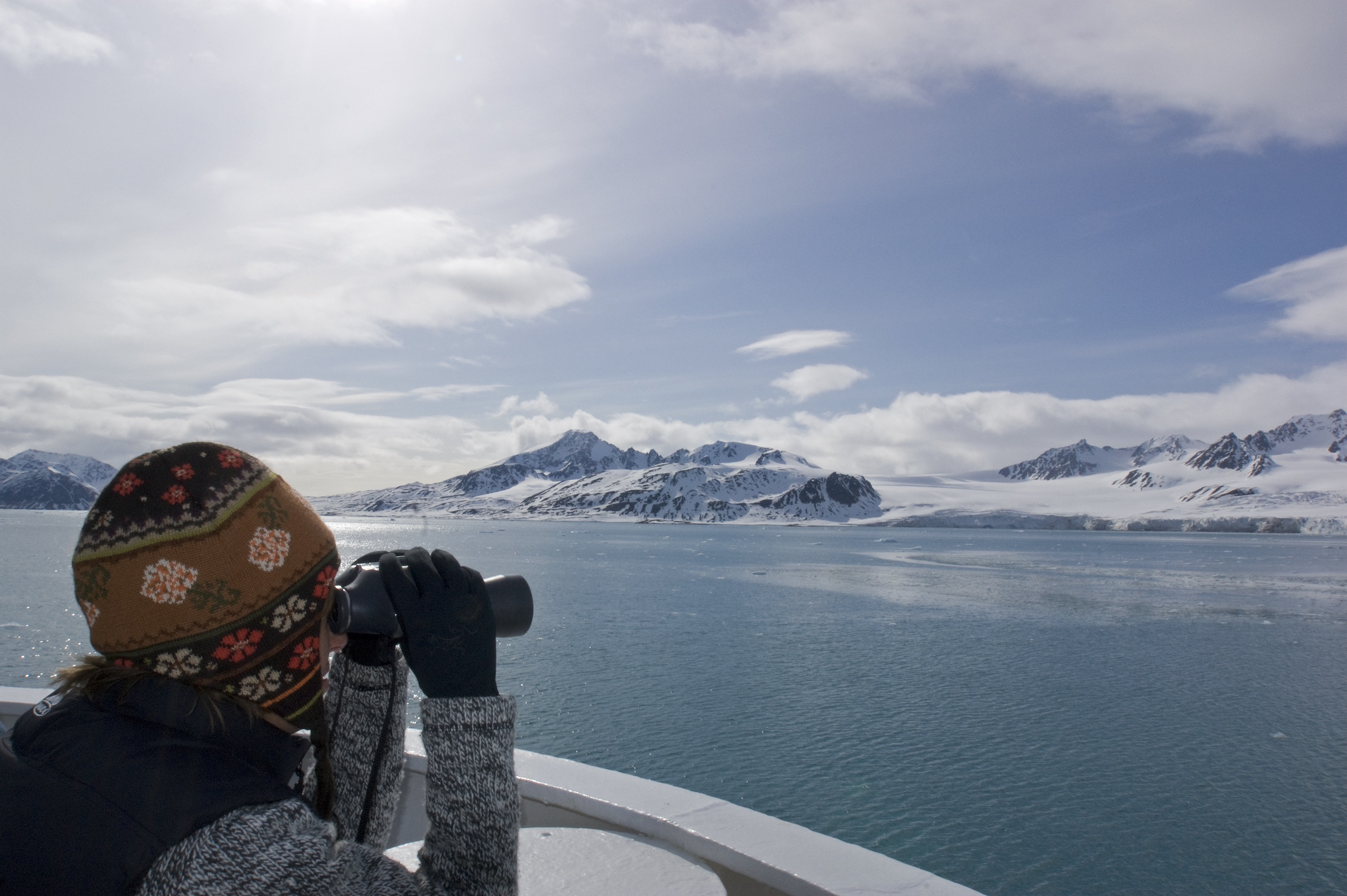 A woman looks through binoculars from the deck of a ship, Svalbard